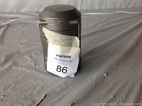 Front view of gray portable LED camping lantern with handle and transparent middle section where LED light visible.