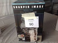 Front and side views of the original box for the Sharper Image Digital Coin Counting Jar, showing product image and branding.
