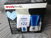 Box and product image front showing Sonic Water Flossing System by CVS Health with product details including 1 base, 1 tank, 2 brush heads, 4 cleaning attachments.