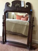 Front view of antique wooden framed mirror reflecting bedroom furniture and decor.