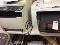 Front and side view of HP OfficeJet Pro 8730 and Canon ImageClass MF5950dw printers side by side on shelf