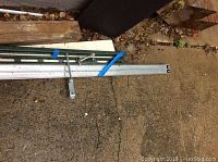 Five metal track pieces laid out on ground, showing length and mounting holes, with a metal clamp attached on one section.