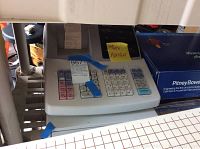 Top and front angle of the Sharp XE-A203 electronic cash register showing keypad and receipt printer with a partially printed receipt.