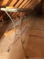 Side view of metal stand table with curved legs and round top showing size and structure.