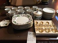 Full view of all teacups, plates, saucers, sugar dish, tea bag dish, and boxed gold-plated teaspoons arranged on table.
