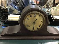 Front view of the Gilbert mantel clock showing face, wooden casing, and missing glass
