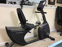 Side view of black Horizon recumbent exercise bike showing large padded seat, backrest, pedals with straps, and digital console on upright post.