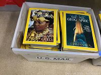 Top view of a white plastic U.S. Mail box filled with National Geographic magazines, showing covers featuring 'African Gold' and 'Beneath the Tasman Sea'.