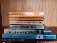 Stack of nine miscellaneous books including Evelyn Waugh novels, John Le Carré novels, James Herriot's Yorkshire, a volume of Robert Bateman's art, and The Egyptian Book of the Dead.