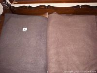 Photo showing two folded brown fleece throws lying side by side on a wooden surface, denoted by a small label with the number 6 on one.
