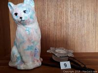 The photo shows a sitting ceramic cat statue with pastel colors next to a white snowflake tealight candle holder.