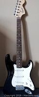 Full-length view of black Squier Stratocaster electric guitar leaning against wall