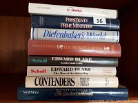 Photo showing seven hardcover history books stacked on a wooden surface.