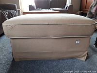 Beige fabric footstool intact, showing overall shape and condition.