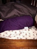 Three folded queen sized sheet sets stacked with a visible number 25 marker. One set is solid dark brown, another is solid purple, and the third has a cream base with brown tree branch and leaf pattern.