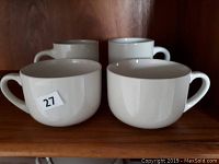 Photo showing 2 large beige coffee mugs and 2 large beige soup bowls arranged on a wooden shelf.