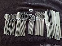 Photo of flatware set laid out on dark fabric background showing knives, dinner forks, teaspoons, soup spoons, and salad forks in even rows.
