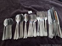 Photo showing the entire flatware set on a dark cloth including knives, dinner forks, salad forks, teaspoons, and soup spoons arranged in groups