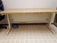 Front view of metal frame supporting wood-grain laminate top table, showing legs, support beam, and laminate surface edge.