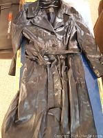 Front side view of a black vintage woman's leather coat showing leather belt and button closure.
