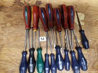 Photo showing 12 assorted screwdrivers with various handle colors and sizes arranged on wooden surface.