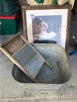 Washboard placed inside metal wash bucket with framed print behind them.