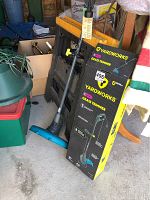 Yard Works grass trimmer standing next to its original box and two black plastic folding saw horses in storage area.