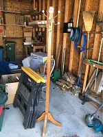 Full view of the wooden coat rack inside a garage, showing the vertical post and base with four legs.