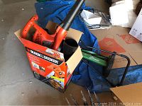 Black & Decker leaf blower inside original box with Scotts Classic push lawn mower in background on floor.