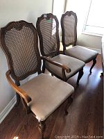 Three wooden dining chairs with cane backrests and beige upholstered seats. Wooden floor background with natural light.