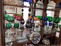 Shelf view showing purple decanter with matching goblets, green and cranberry compote bowl