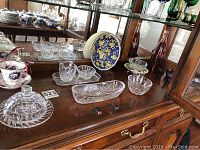 Wide view of crystal glassware collection including covered dish, various bowls, and decorative plate on wooden sideboard with mirror.