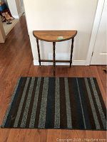 Front view of a semi-circular wooden table with turned legs on wooden floor against white wall.