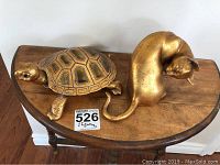 Photo showing both the gold-colored metal cat and turtle figurines placed on a wooden surface.
