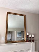 Front view of mirror hanging on wall with three red wooden candle sticks on mantle below
