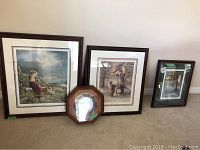 Three framed prints and one decorative plate displayed leaning against wall on carpeted floor.