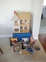 Front view of the wooden dollhouse sitting on a blue plastic bin with various accessories and dollhouse items arranged in front.