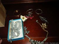 Photo displaying assorted costume jewelry including rhinestone necklace and bracelet, several brooches in floral and leaf designs on a dark wooden surface