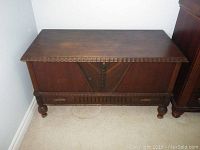 Front view of wooden storage chest showing carved details and angled panels with a dark stain finish.