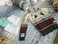 Photo displaying the HBC knit sweater with reindeer and leaf patterns alongside four pieces of baby clothing including tops and bottoms in pastel colors.