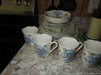 Porcelain dishes and mugs with blue floral pattern, stacked on countertop.