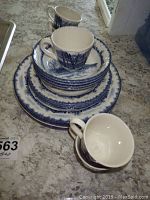 Stacked plates, bowls, and two tea cups showing blue winter tree scenic pattern on white ceramic.