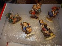 Overview of five Hummel figurines in a box on bubble wrap, showing various poses and colors.