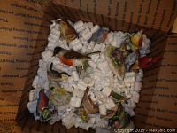 Top view of all eight porcelain bird figurines nestled in shipping peanuts inside a box showing colorful hand-painted details.