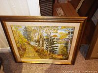 Full view of the framed oil on board painting showing a lakeside path with trees and a canoe, framed in gold.