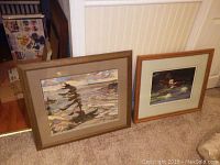Photo of two framed prints leaning against wall on carpet floor. One depicts a tree with a scenic water background; the other a duck with lily pads.