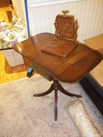 Wood drop leaf table with two extendable leaves and pedestal base, photo showing closed leaves with vanity organizer on top.