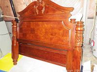 Full view of wood poster bed with ornate headboard and footboard showing carved floral details, turned posts, and panel construction.