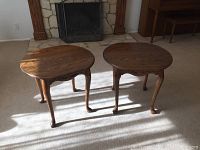 Two oak end tables shown together in front of a fireplace on a carpeted floor, highlighting the tops, legs, and aprons.