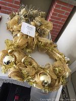 Two gold Christmas wreaths placed side by side, showing mesh ribbons, gold ornaments, pinecones, and gold tinsel detail